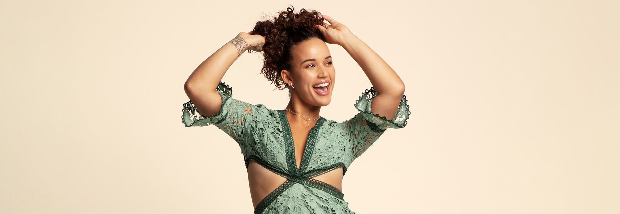 A young woman striking a pose while wearing a green lace top with cutout details
