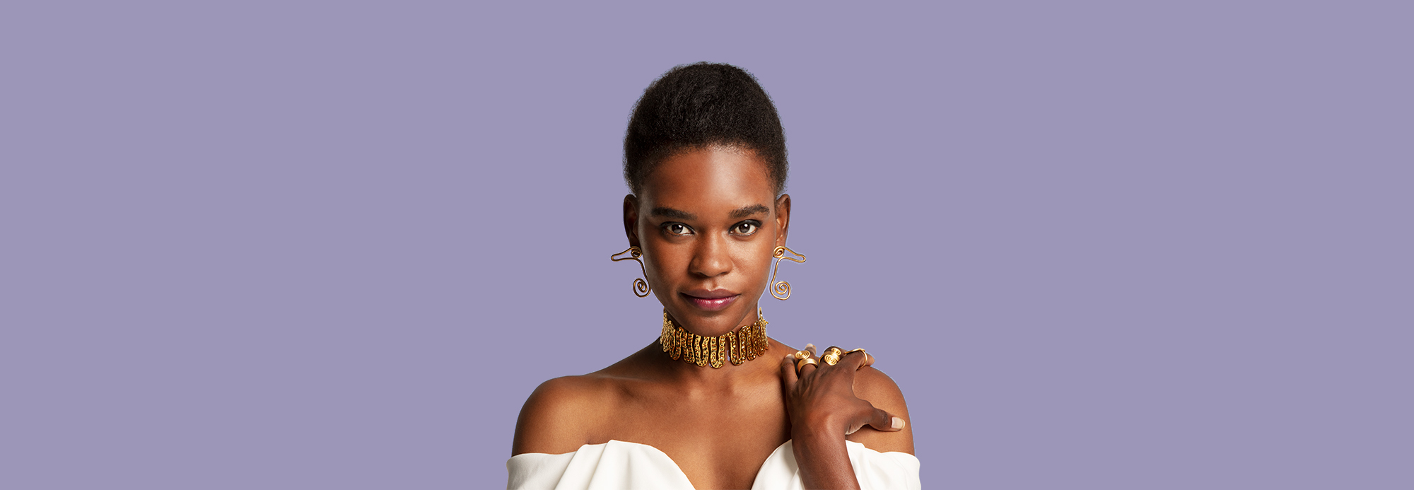 A woman wearing statement earrings, ring, and necklace and a strapless top